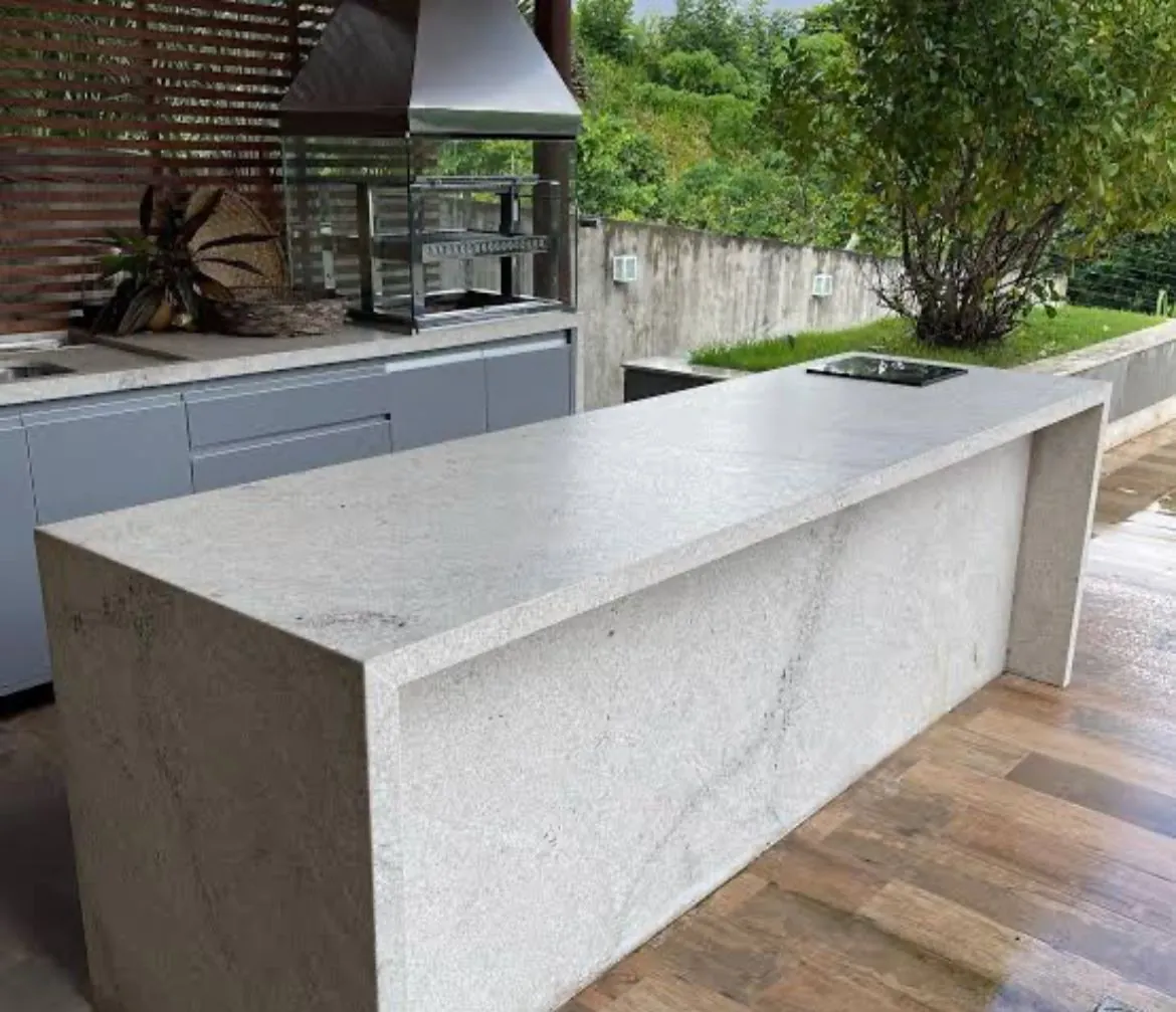 Bancada de área gourmet em granito branco com churrasqueira ao fundo